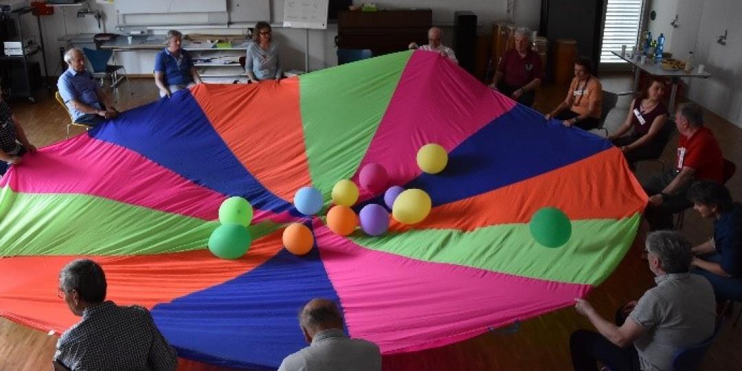 Kursteilnehmende sitzen mit Kursleiterinnen in einem Kreis; Tuch dazwischen gespannt mit Balloonen (Foto: Daniela Brunner)