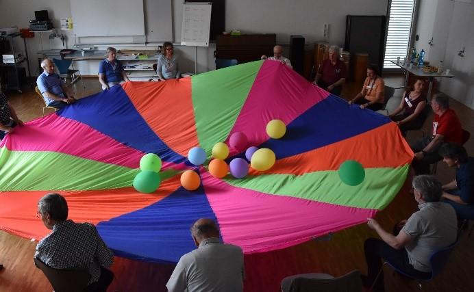 Kursteilnehmende sitzen mit Kursleiterinnen in einem Kreis; Tuch dazwischen gespannt mit Balloonen (Foto: Daniela Brunner)